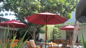 An outdoor patio with wooden tables and chairs, red umbrellas, and a water feature.