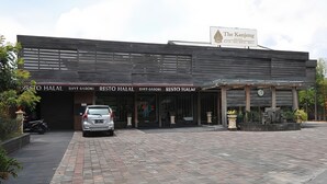 A building with a sign for The Kanjeng Suites, indicating it is a hotel. There are two entrances labeled "XTO HALAL" and "RESTO HALAL". A car is parked in front.