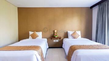 A hotel room with two beds, a wooden headboard, a small shelf with a vase, and a window with curtains.
