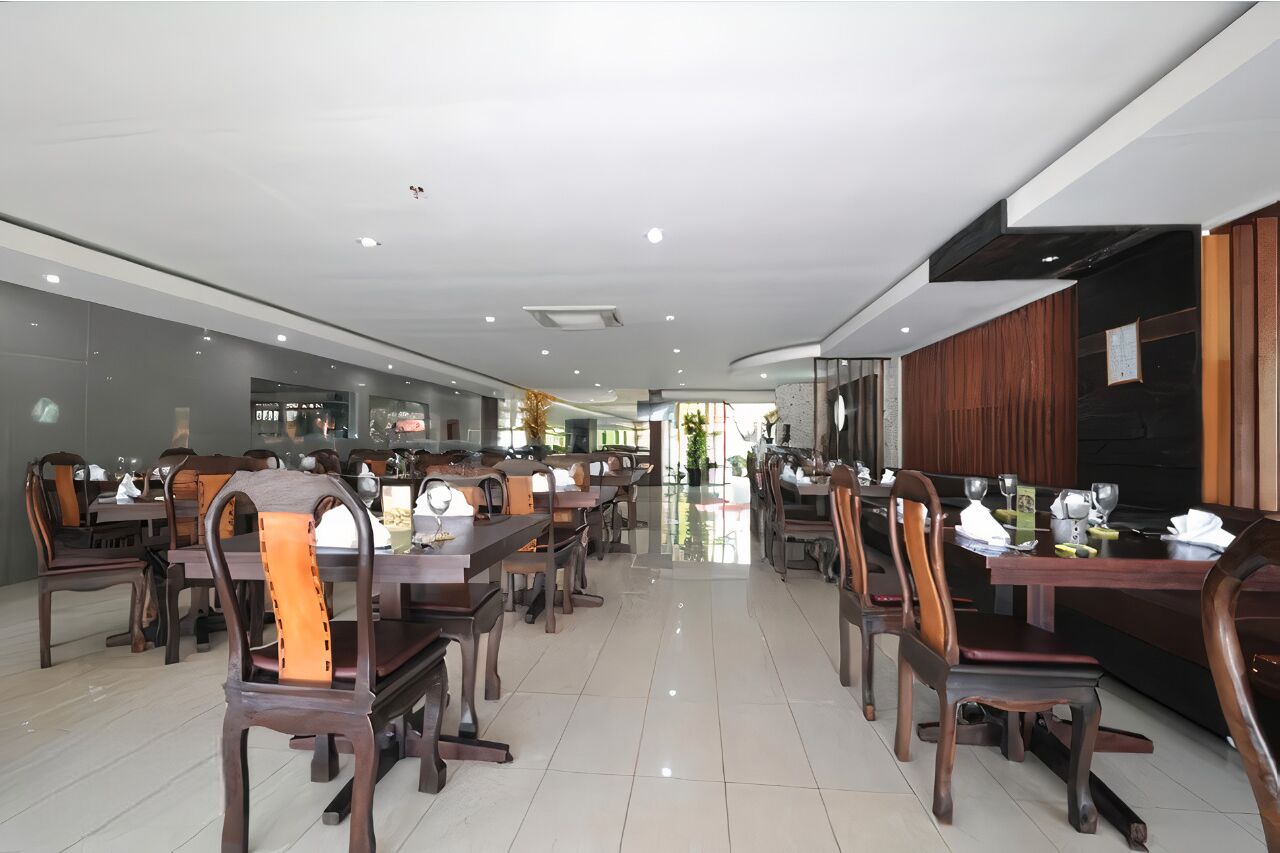 Un vaste espace dédié à la salle à manger, avec de nombreuses tables et chaises, un design moderne au niveau du plafond et une vue sur le restaurant en arrière-plan.