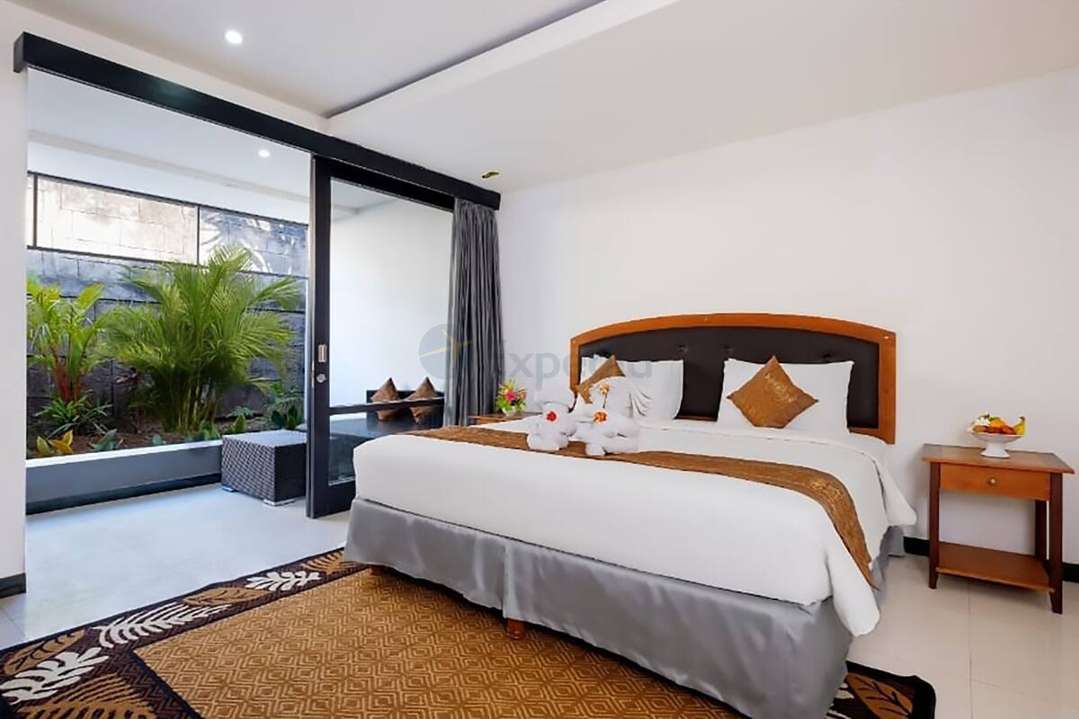 A modern hotel room with a large bed, a small side table, and a view of a garden through a sliding door.