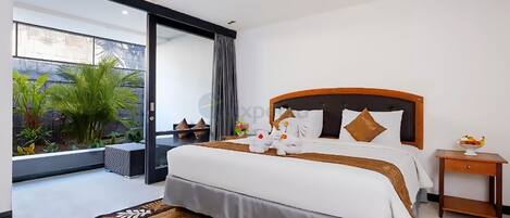 A modern hotel room with a large bed, a small side table, and a view of a garden through a sliding door.
