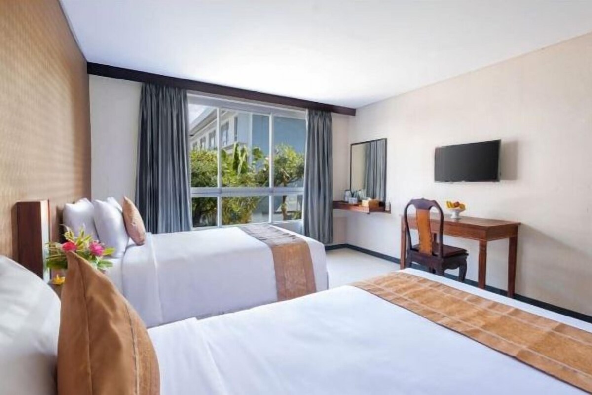 A hotel room with two beds, a desk, a chair, a TV, and a large window with curtains.