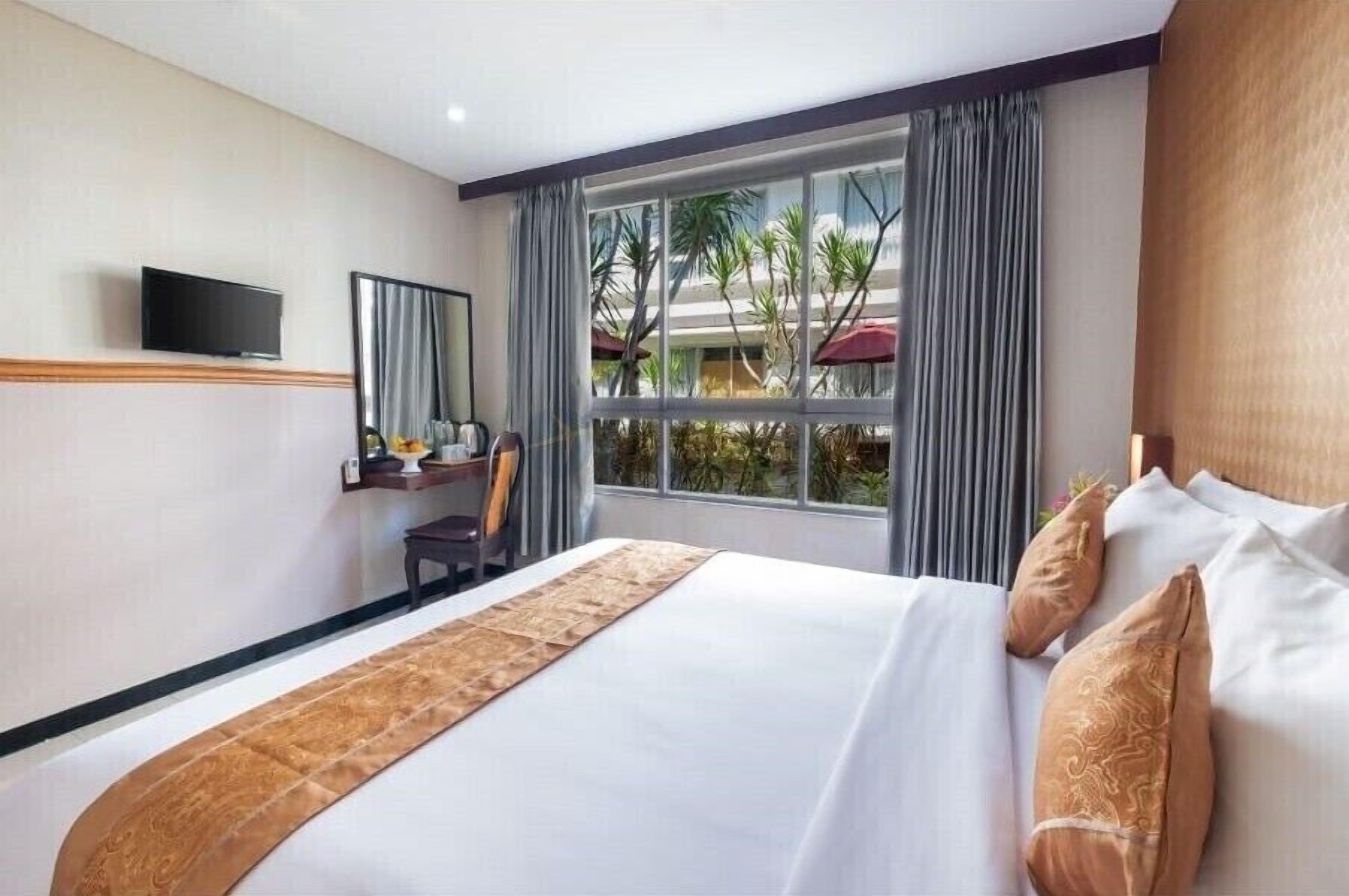 Una habitación de hotel con una cama grande, un escritorio con silla, un televisor y una ventana con cortinas.