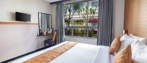Una habitación de hotel con una cama grande, un escritorio con silla, un televisor y una ventana con cortinas.