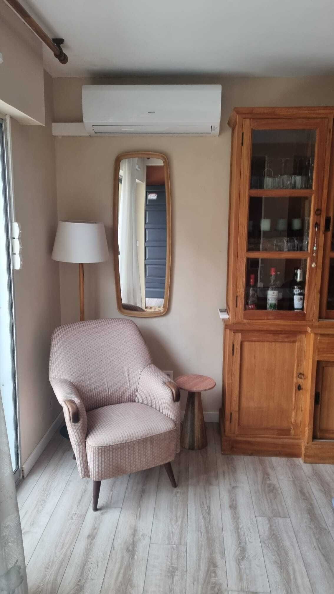 Ein Zimmer mit einem Korbsessel, einem kleinen runden Tisch, einem Spiegel und einer Holzkommode mit Glastüren.