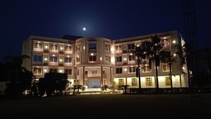 A multi-story hotel with a central courtyard, illuminated windows, and a moon in the sky.