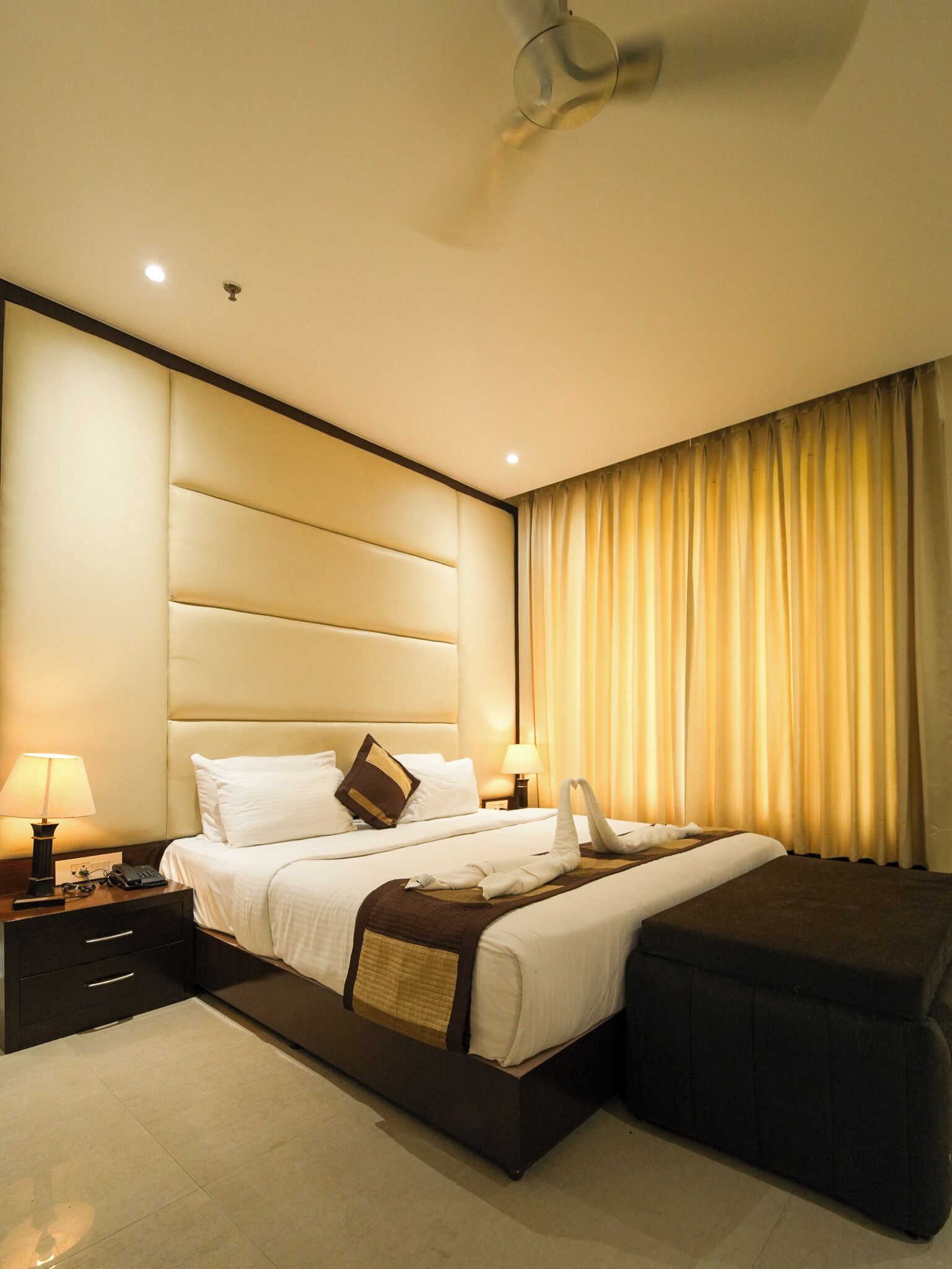 Une chambre d’hôtel avec un grand lit, des lampes de chevet, un téléphone, une table de chevet et un ventilateur de plafond.