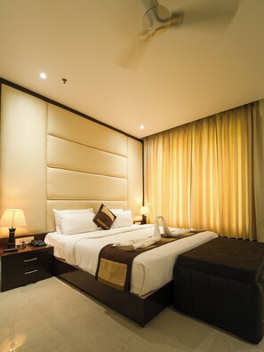 Habitación de hotel con una cama grande, lámparas de noche, un teléfono, una mesita de noche y un ventilador de techo.