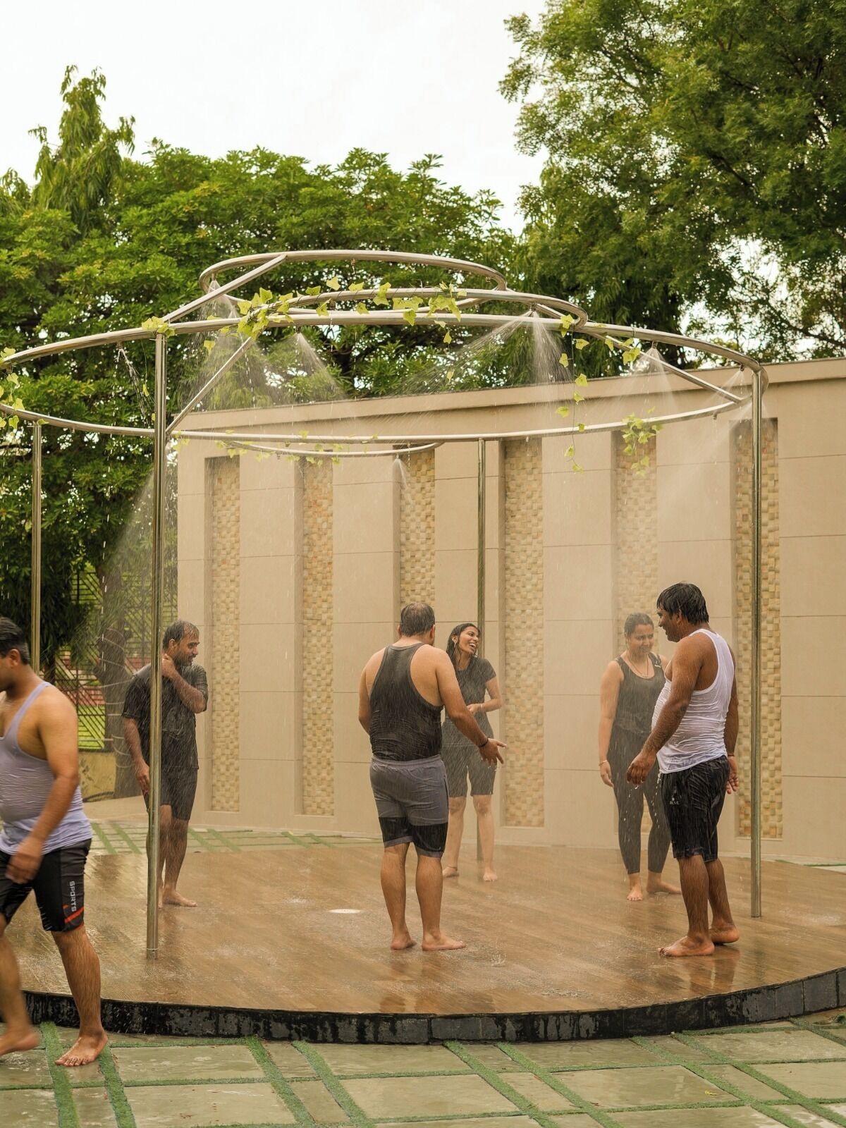 Un groupe de personnes se tient sous une fontaine ou un autre élément décoratif aquatique, dans un espace extérieur.
