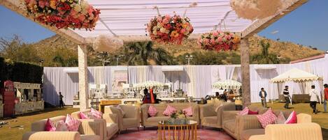 An outdoor event space with a covered seating area, tables, and hanging floral arrangements.