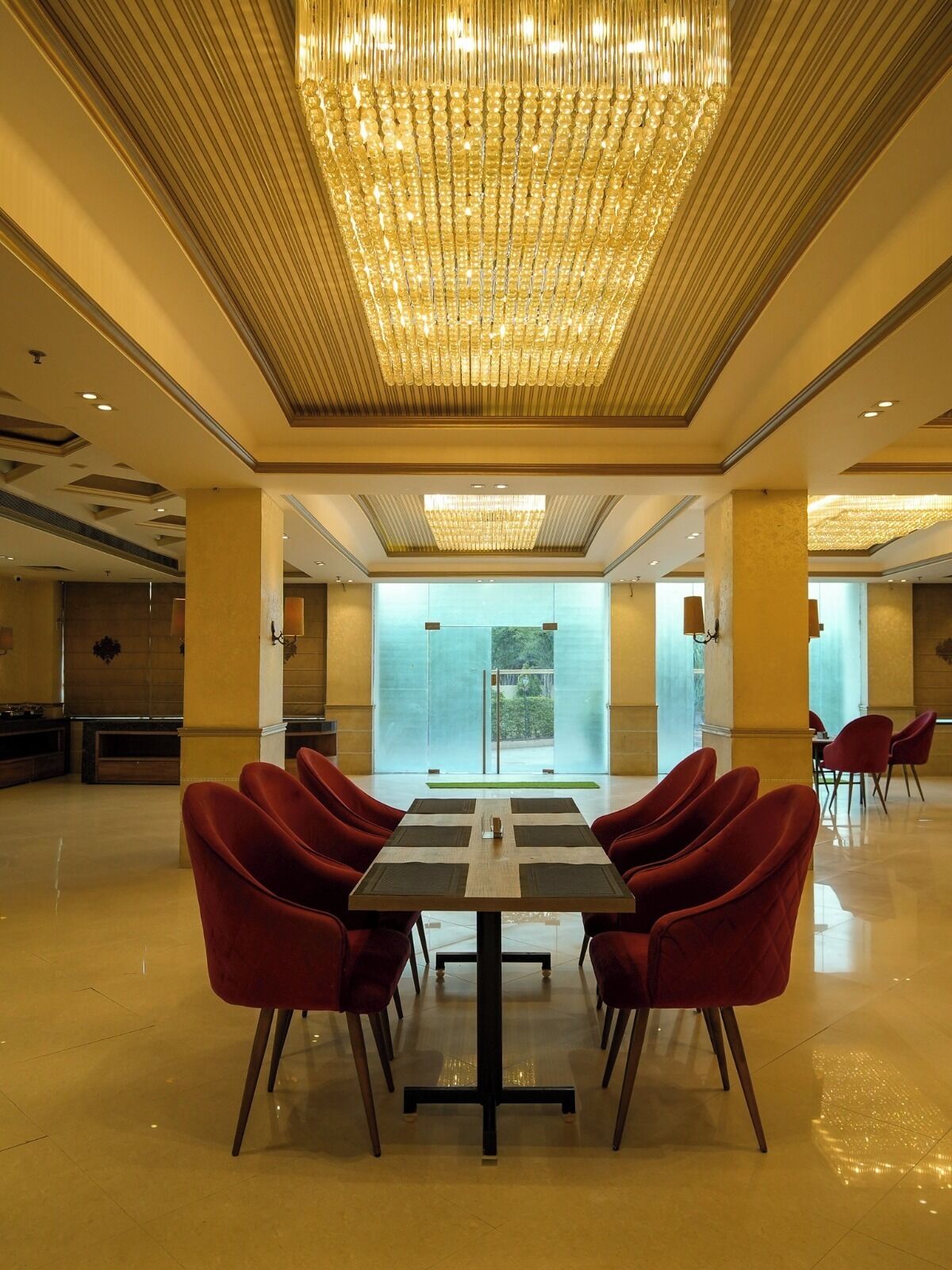 Un hall d’entrée spacieux, agrémenté d’un grand lustre, de fauteuils rouges, d’un comptoir d’accueil et d’un mur de verre offrant une vue dégagée.