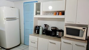 A compact kitchen with white cabinets, a blue door, and basic appliances including a refrigerator, coffee maker, and microwave.