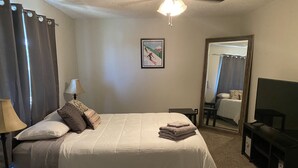 A neatly made bed with pillows, a bedside lamp, a framed picture on the wall, a mirror, and a TV on a stand. - Cozy 2-bedroom condo close to both Denver and the Mountains (Denver)