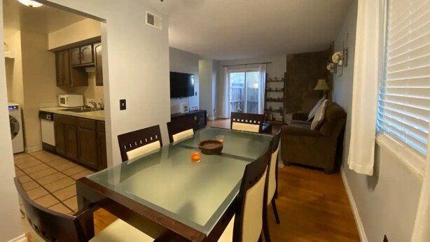 A dining area with a glass-top table, wooden chairs, a ceiling fan, and a kitchen in the background. - Cozy 2-bedroom condo close to both Denver and the Mountains (Denver)