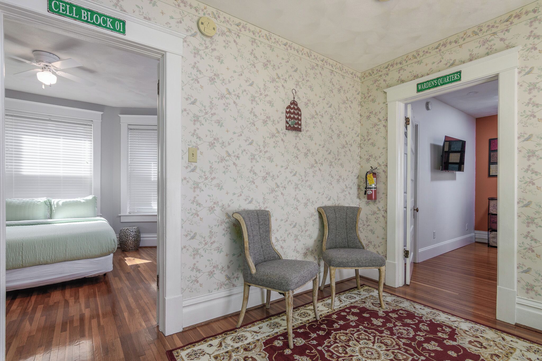 Ein Zimmer mit einem Bett, zwei Stühlen, einer Wand mit Muster und einer Tür mit der Aufschrift "WARDEN'S QUARTERS".