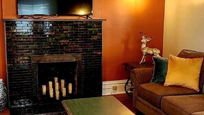 Una sala de estar con chimenea de ladrillo, un televisor de pantalla plana montado encima, un sofá con cojines y una estatua decorativa de un ciervo.