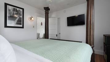 Un dormitorio con cama, un cuadro enmarcado, televisor y una puerta.