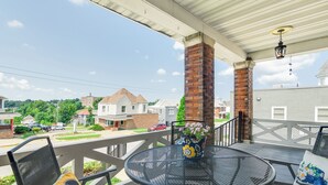Un patio techado al aire libre con una mesa redonda y sillas, una planta en maceta y vistas a un barrio residencial.