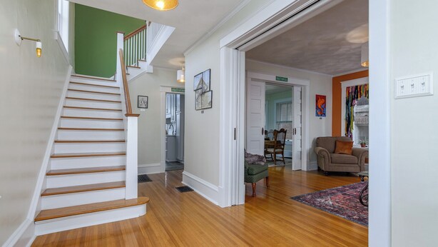 Una escalera con escalones de madera y paredes blancas que conduce a una habitación con una pared verde y una puerta que indica “Habitación de Huéspedes”.