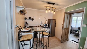 Une cuisine compacte avec une table ronde en verre, deux tabourets de bar, un réfrigérateur et un four à micro-ondes.