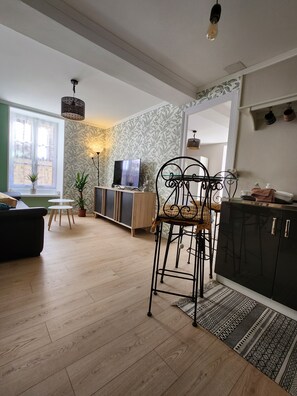 Un salon moderne comprenant un canapé, une table à manger avec des chaises, un téléviseur et un coin cuisine avec des placards et un plan de travail.