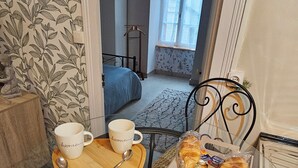 Une pièce confortable avec un lit, une fenêtre, une table à manger avec une tasse et une soucoupe, et une chaise.