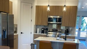Et moderne køkken med en central ø, barstole, indbygget ovn og køleskab.