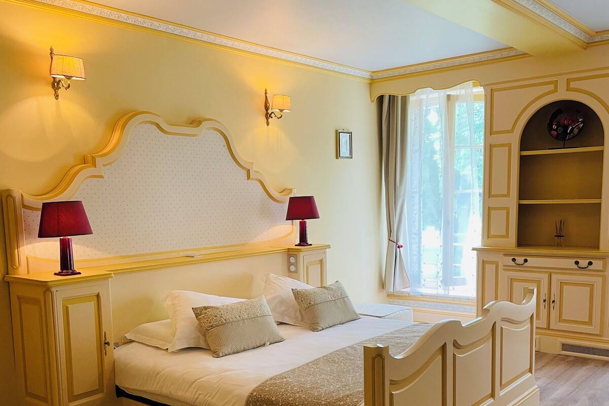 Une chambre à coucher comprenant un lit, deux lampes de chevet, une table de chevet, une commode et une fenêtre avec des rideaux.