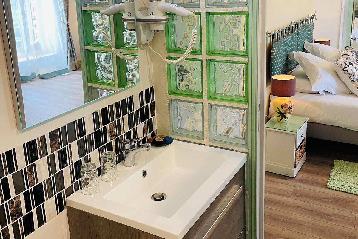 Une salle de bain avec un lavabo blanc, un miroir et un mur orné d’un motif vert.