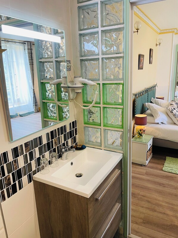 A bathroom with a white sink, a mirror, and a green patterned wall. - Hôtel & Events du Château Lacaze (Aiguillon)