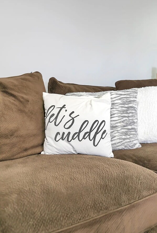 Un sofá marrón con un almohadón blanco que dice 'Let's cuddle'.