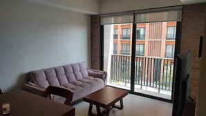 A living room with a sofa, a small table, and a TV. There is a large window with a view of a building outside. - Country GDL 1parking/2br/2ba (Guadalajara)