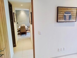 Un couloir mène à une salle à manger où se trouvent une table et des chaises, un tableau au mur et une porte sur la gauche.