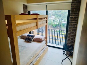 Un lit superposé donnant sur une rue et des arbres, avec vue depuis un balcon.