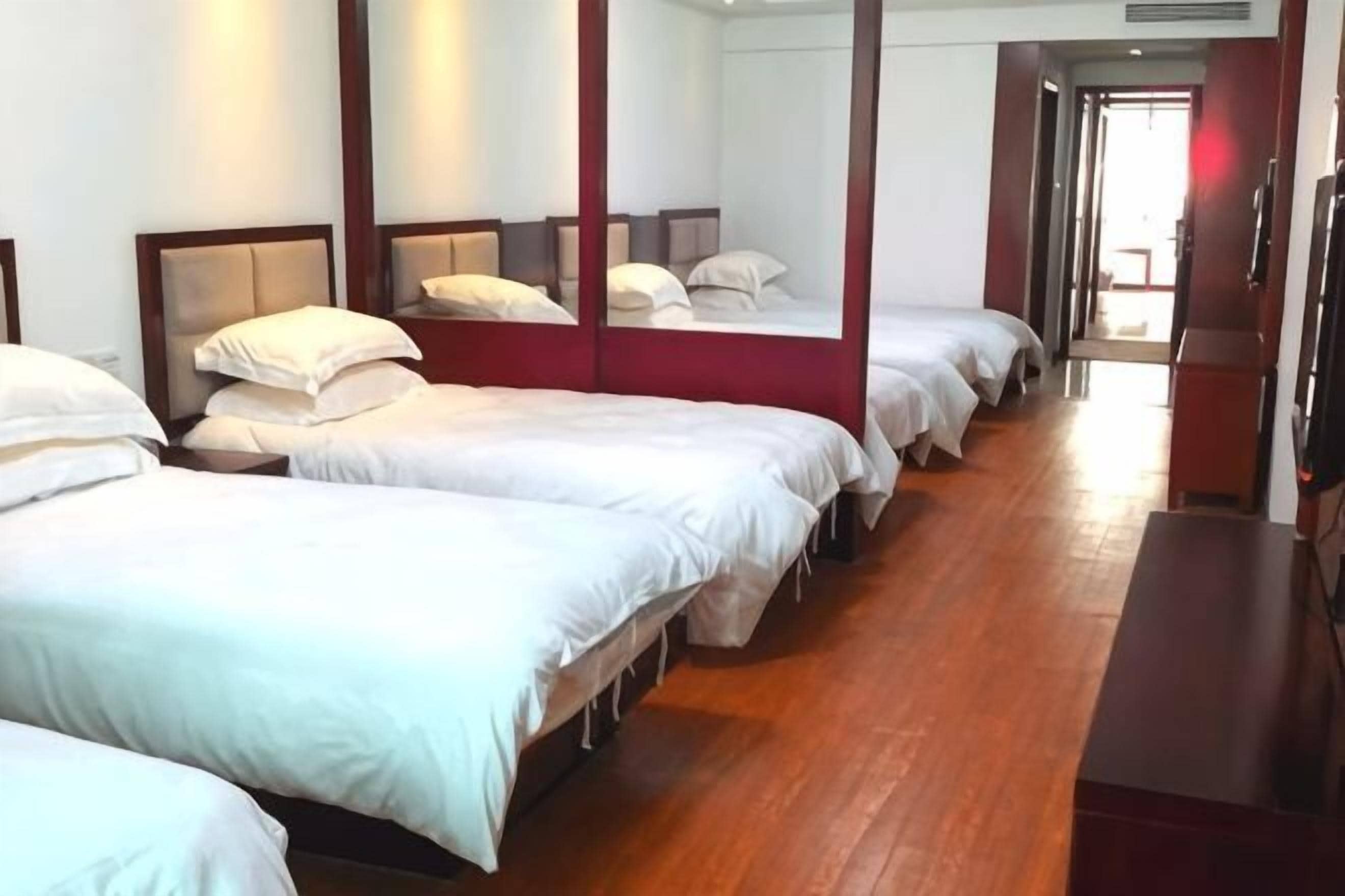 A hotel room with four beds arranged in a row, a wooden floor, and a large mirror on the wall.