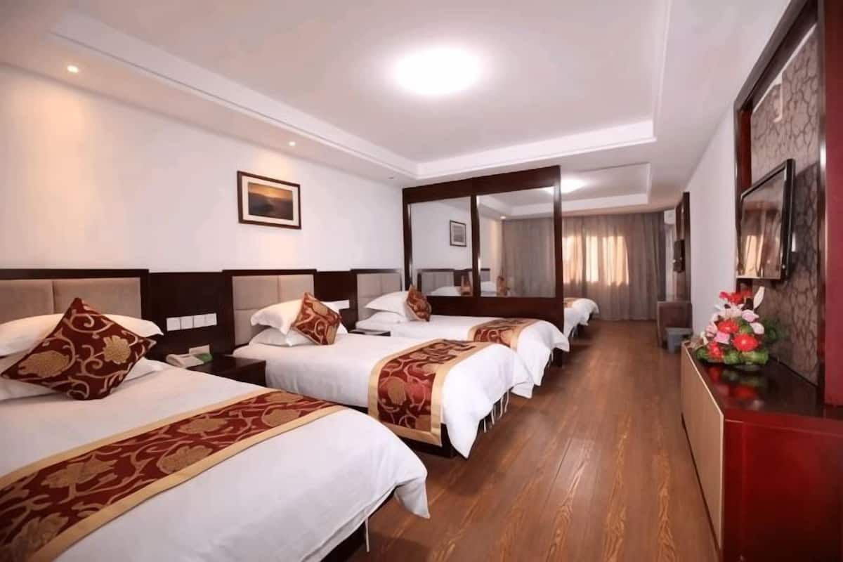 Habitación de hotel con tres camas, suelo de madera, un escritorio con un florero y un espejo grande.