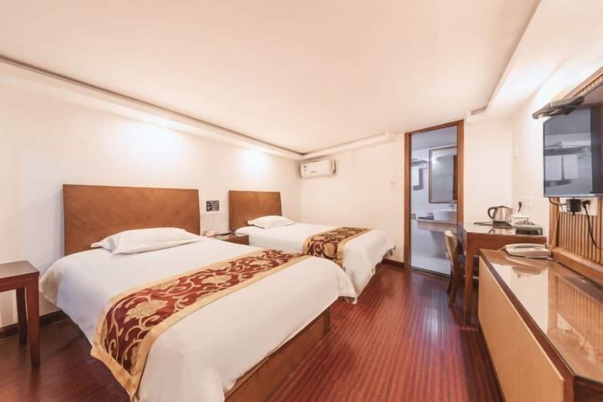 Habitación de hotel con dos camas, cabecero de madera, escritorio con espejo y televisión.