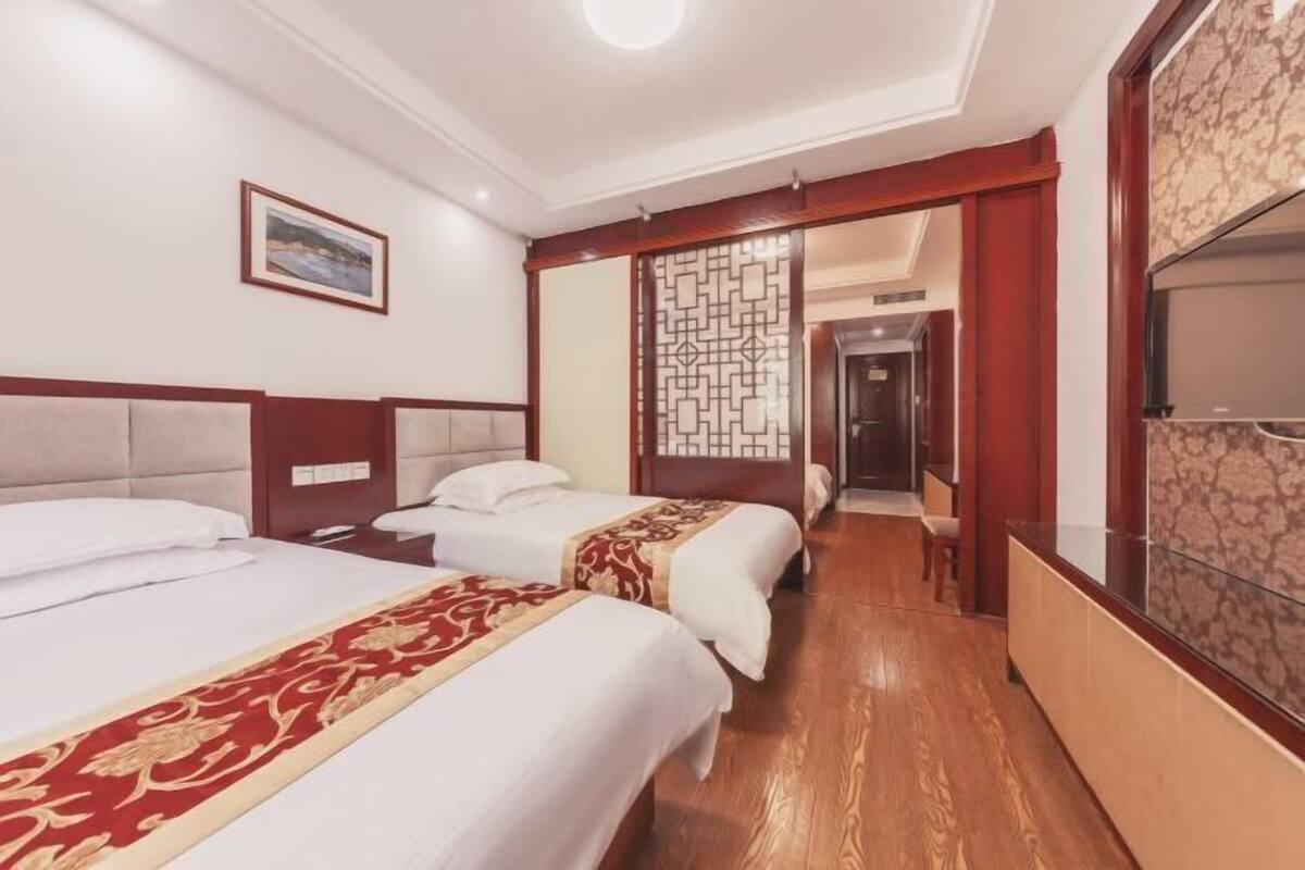 Habitación de hotel con dos camas, suelo de madera, un separador decorativo y un cuadro en la pared.
