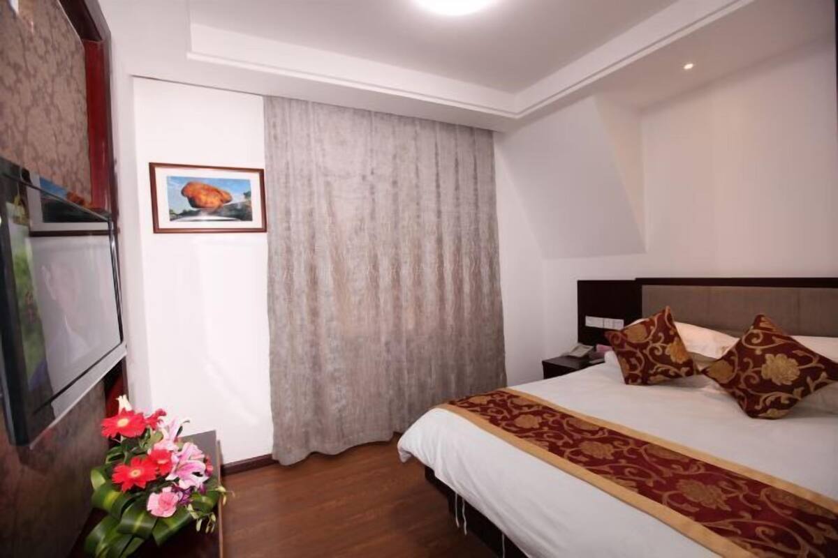 Una habitación de hotel con una cama, una mesita de noche, un televisor, una cortina y un cuadro en la pared.