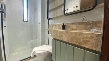 Um banheiro moderno com chuveiro em gabinete de vidro, vaso sanitário e toucador com bancada de mármore.