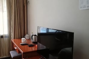 A hotel room with a wooden desk, a flat-screen TV, a coffee maker, a cup, and a smartphone.