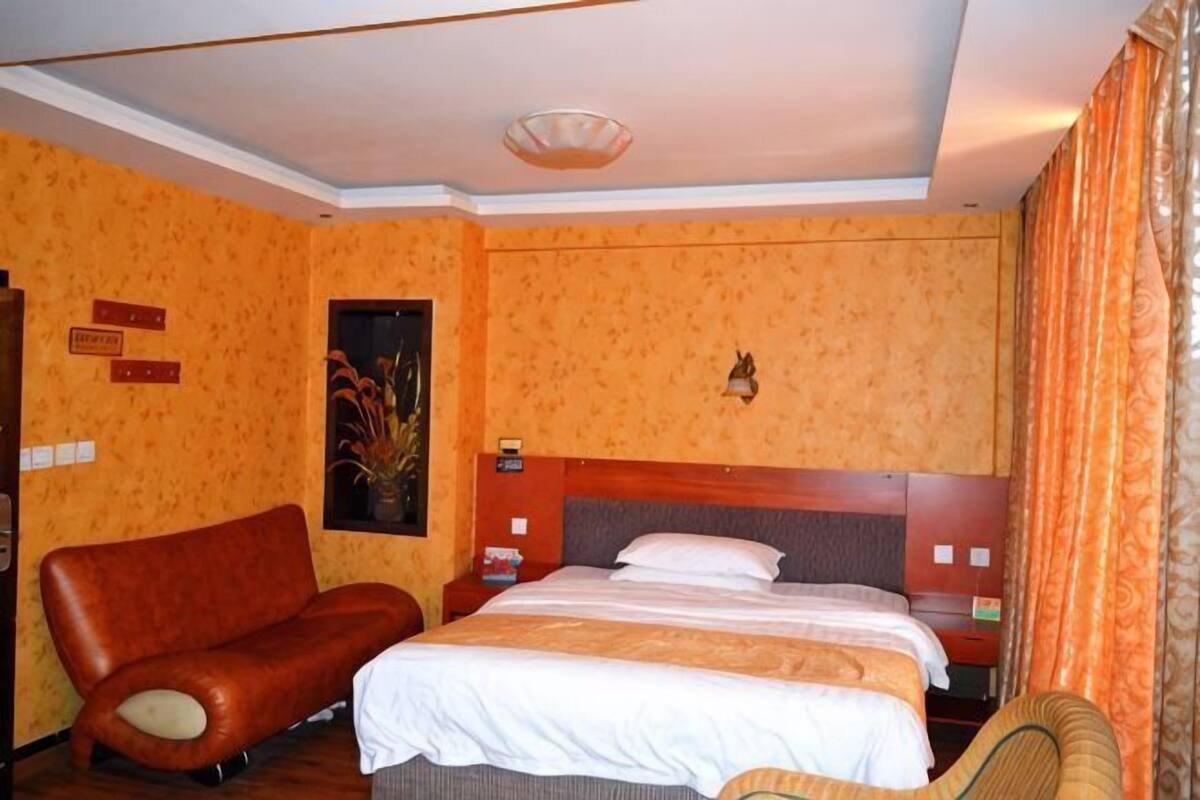 Une chambre d’hôtel avec un lit, un canapé, une table de chevet et une lampe fixée au mur.