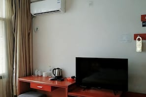 A room with a desk, a television, an air conditioner, and a window with curtains.