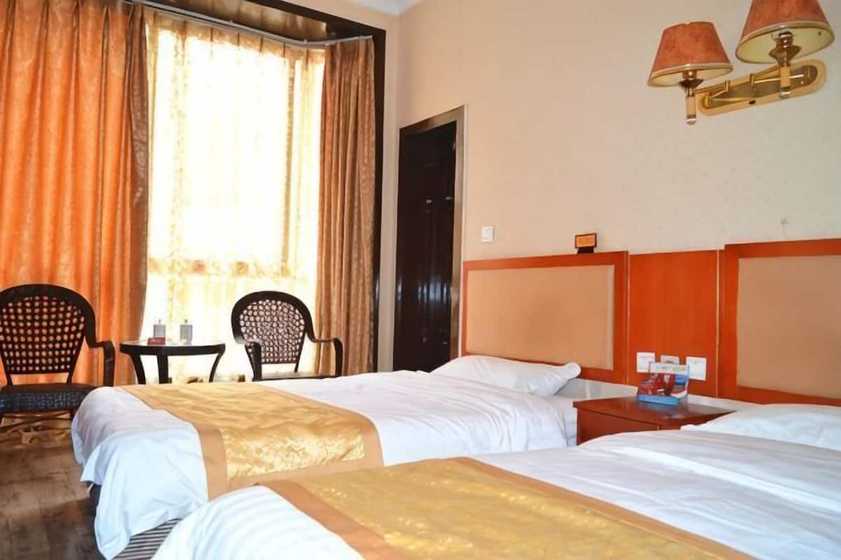 A hotel room with two beds, a sitting area with chairs, a table, and a lamp.