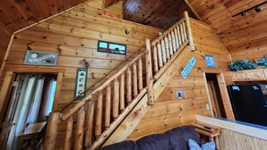 Puinen mökki sisältä, jossa on portaikko, tervetulotoivotus, kyltti, joka osoittaa majapaikkaan, ja musta jääkaappi.