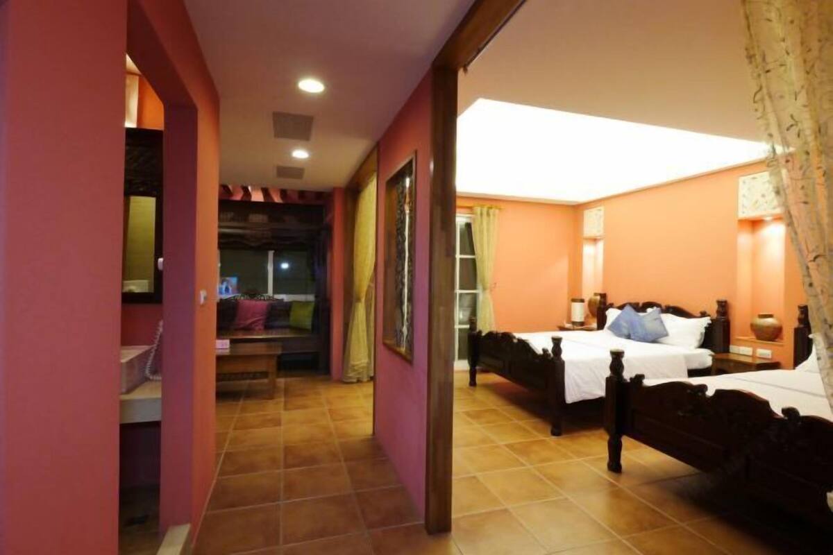A hotel room with a large bed, a desk, and a chair. There is a bathroom with a shower and a toilet. The room has a tiled floor and a window with curtains.