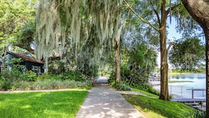 A pathway leading to a rustic cabin surrounded by lush greenery and a lake. - Elegant Lake Retreat (Mount Dora)