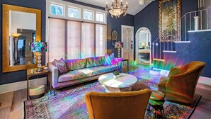 A living room with a sofa, chairs, a coffee table, and a chandelier. There is a large window and a door leading to another room. - Elegant Lake Retreat (Mount Dora)
