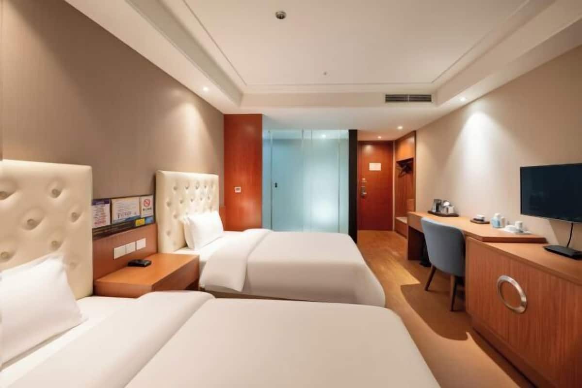Habitación de hotel con dos camas, un escritorio, una silla, un televisor y un armario de madera.